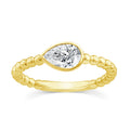 A yellow gold ring featuring a pear-cut clear gemstone in a bezel setting, mounted on a twisted beaded gold band, shown against a plain white background.