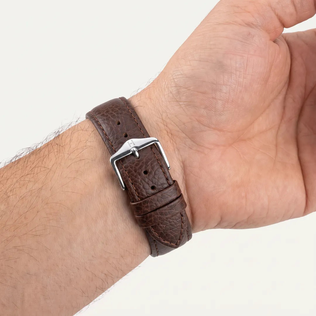 Hirsch Kansas brown buffalo-embossed calf leather watch band worn on a male wrist, inner-wrist view showing the steel pin buckle