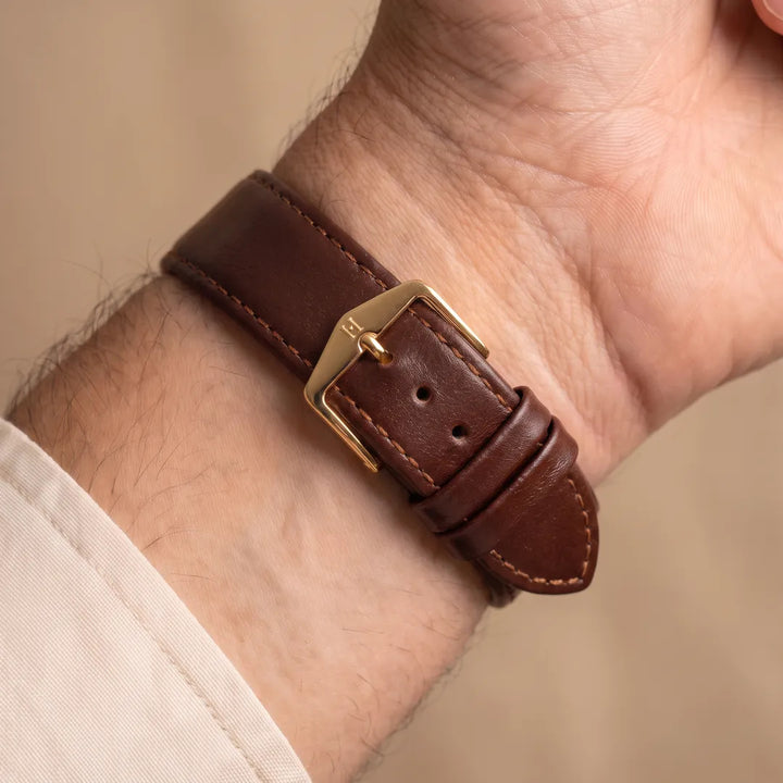 Osiris brown calf leather watch band worn on a man's wrist, inner-wrist view showing the gold pin buckle