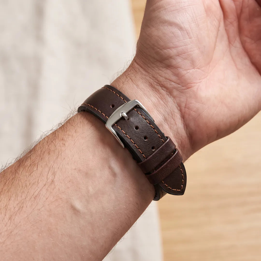 Hirsch James brown calf leather performance watch band worn on a man's inner wrist, showing leather upper with tan contrast stitching and polished steel buckle