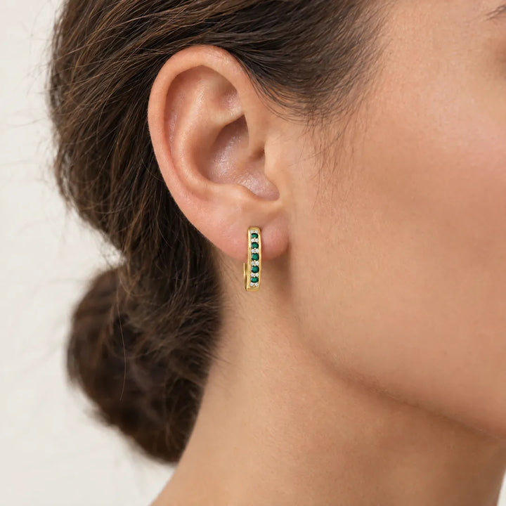 Small 9K yellow gold huggie hoop earring set with emeralds and diamonds, worn on a model's ear