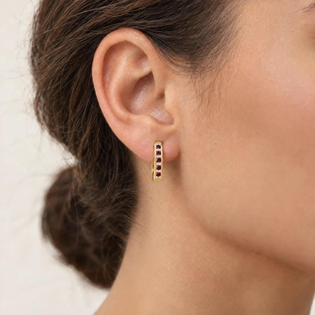 Small 9K yellow gold huggie hoop earring set with rubies and diamonds, worn on a model's ear