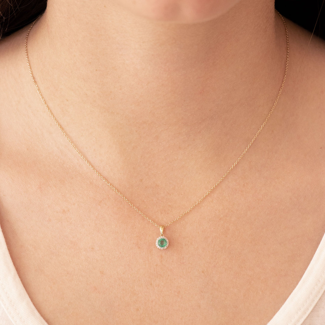 Gold necklace with a green gemstone pendant on a person wearing a white top.