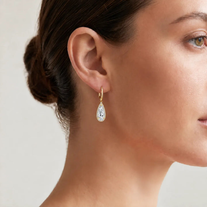 Woman wearing a 5.37ct elongated pear lab grown diamond halo drop earring in 18K yellow gold on a leverback, close-up on the ear