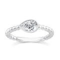 A silver ring featuring a marquise-cut clear gemstone in a bezel setting, with a beaded band, shown on a plain white background.
