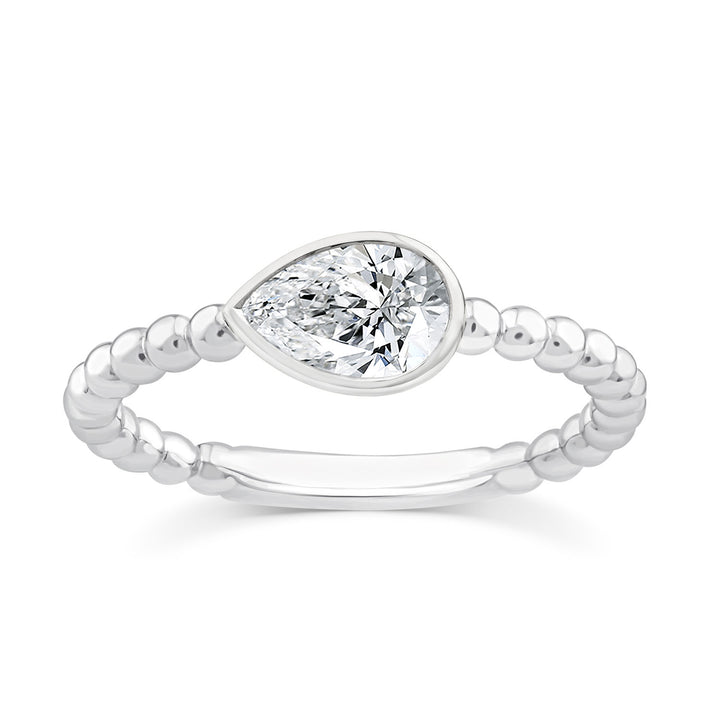 A silver ring featuring a marquise-cut clear gemstone in a bezel setting, with a beaded band, shown on a plain white background.