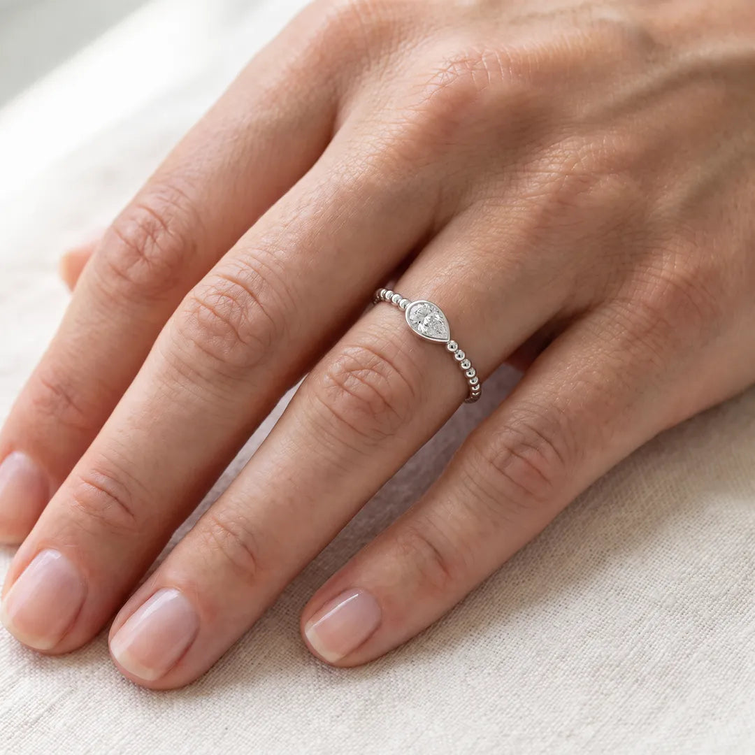 0.50ct pear lab grown diamond bezel ring with beaded band in 9K white gold, worn on a woman's ring finger