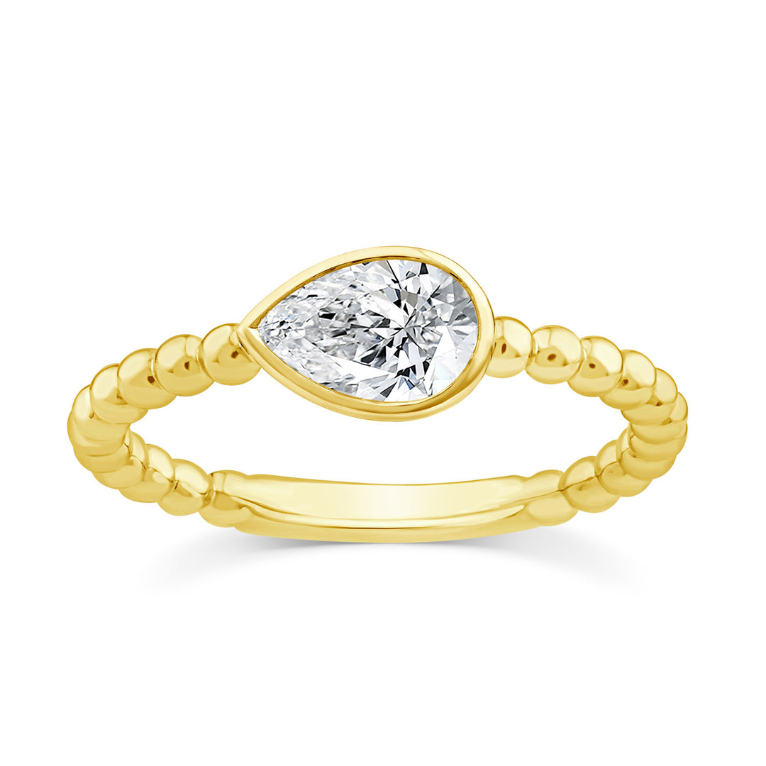 A yellow gold ring featuring a pear-cut clear gemstone in a bezel setting, mounted on a twisted beaded gold band, shown against a plain white background.