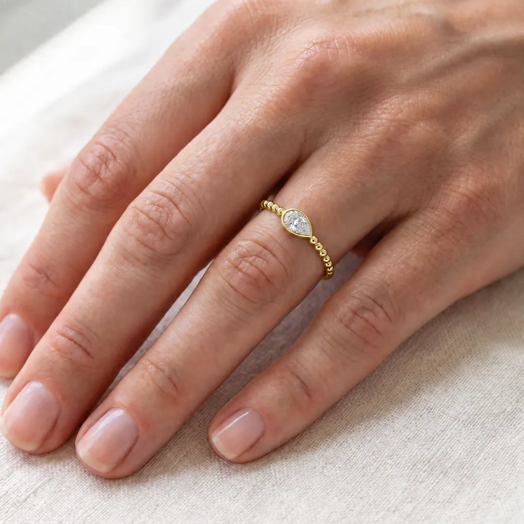 0.50ct pear lab grown diamond bezel ring with beaded band in 9K yellow gold, worn on a woman's ring finger