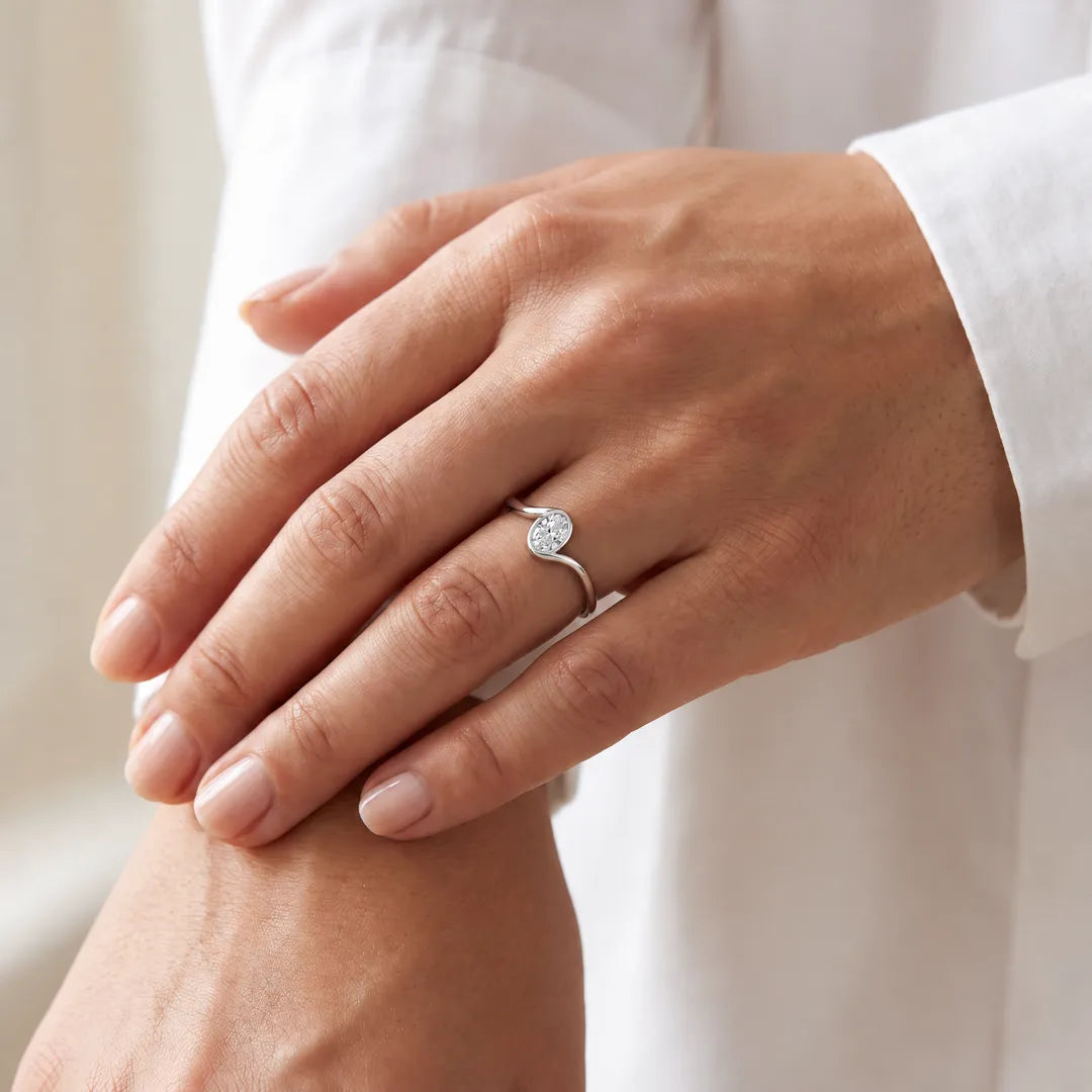 1.00ct oval lab grown diamond bezel-set offset ring in 9K white gold worn on a model's hand