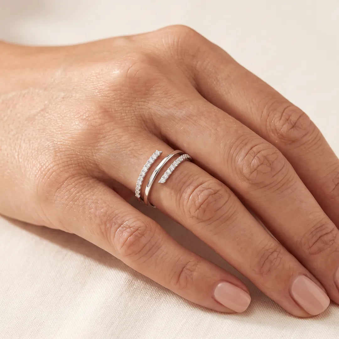 Close-up of a woman's hand wearing the 0.25ct lab grown diamond wrap ring in 9K white gold on her ring finger, resting on cream linen.