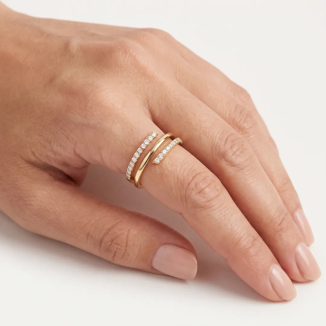 A slim yellow gold diamond wrap ring worn on a woman's middle finger, two bands set with rows of round-cut diamonds, against a soft off-white background.