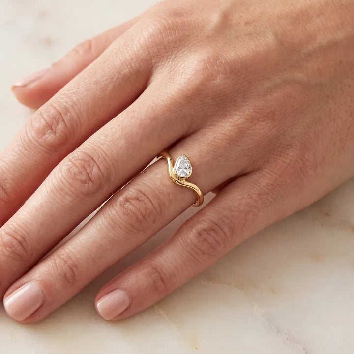 0.50ct pear lab grown diamond offset ring in 9K yellow gold worn on a woman's ring finger