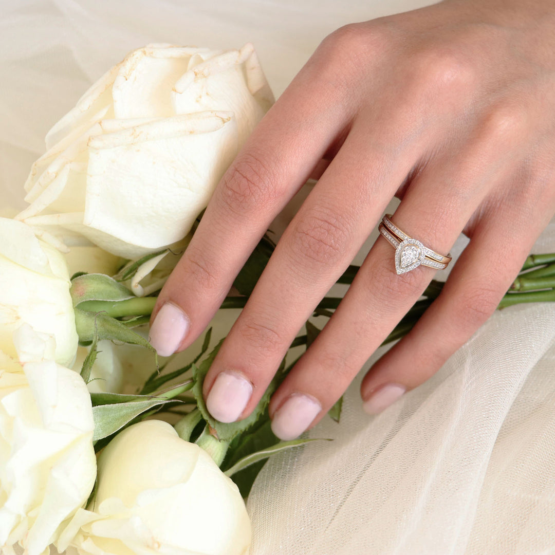 Hand wearing a pear-shaped diamond ring set in 9K yellow gold, with white roses.